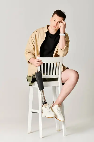 Um homem bonito com uma perna protética confiantemente se senta em cima de uma cadeira branca. — Fotografia de Stock