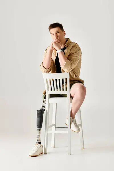 A handsome man with a prosthetic leg showcases dynamic poses on a white chair. — Stock Photo