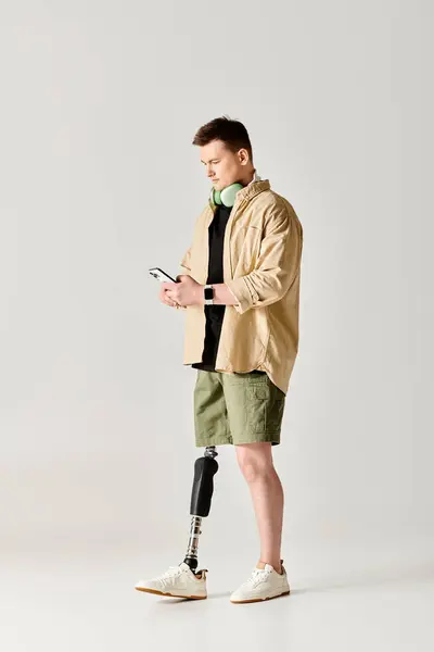 Um homem bonito com uma perna protética em uma jaqueta bronzeada usa um smartphone. — Fotografia de Stock