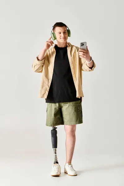Un hombre con una pierna protésica usando auriculares y sosteniendo un teléfono celular. - foto de stock