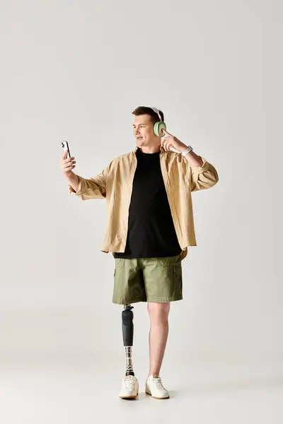 Un bel homme avec une jambe prothétique, portant une chemise noire et un short kaki, tient un téléphone portable. — Photo de stock