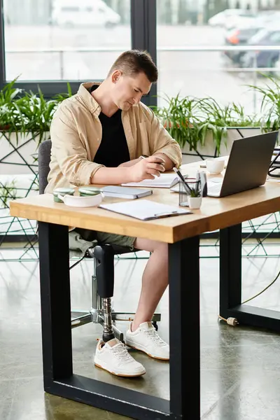 Ein gutaussehender Geschäftsmann mit Beinprothese arbeitet an einem Laptop am Tisch. — Stockfoto
