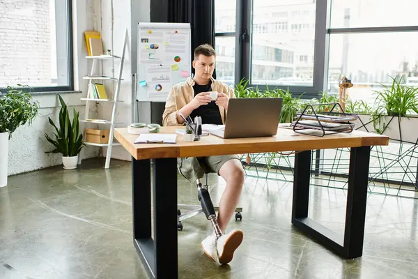 Un hombre de negocios guapo con una pierna protésica trabajando diligentemente en un escritorio usando un portátil. - foto de stock