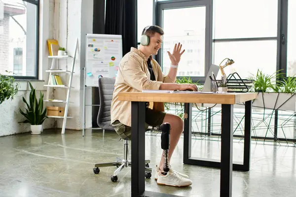 A handsome businessman with a prosthetic leg sitting at a desk, wearing headphones. — Stock Photo