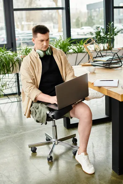 A handsome businessman with a prosthetic leg, engrossed in working on his laptop in an office chair. - foto de stock