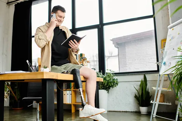 Un bel homme d'affaires avec une prothèse de jambe est assis à une table, parlant sur un téléphone portable. — Photo de stock