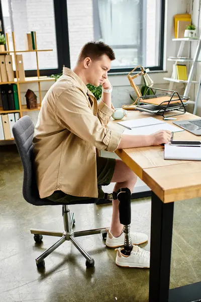 Красивый бизнесмен с протезной ногой глубоко в работе на ноутбуке за своим столом. — стоковое фото