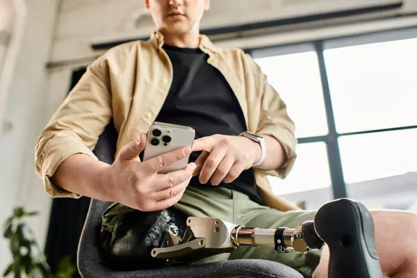 A handsome businessman with a prosthetic leg sitting in a chair, focused on his cell phone. — Stock Photo