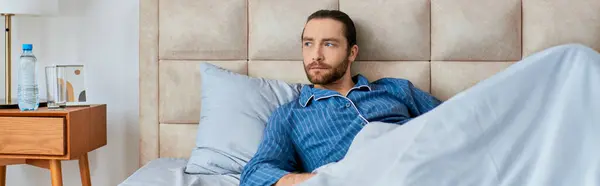 Un uomo sdraiato a letto, drappeggiato in un lenzuolo, rilassante e rigenerante. — Foto stock