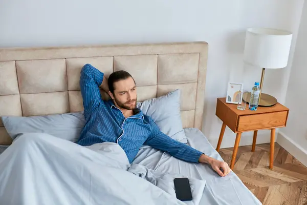 Un hombre se acuesta en la cama, teléfono cerca de la mano. - foto de stock