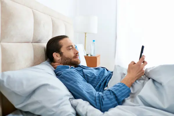 Un hombre comprueba pacíficamente su teléfono mientras está acostado en la cama. - foto de stock