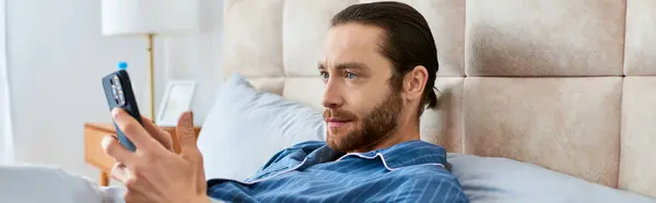 A man relaxing in bed, practicing mindfulness with his cell phone in hand. — Stock Photo
