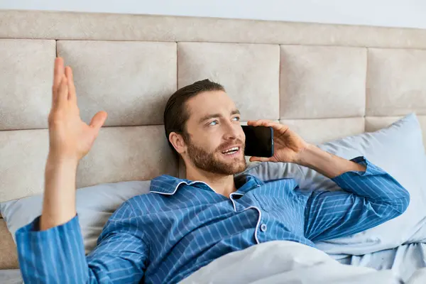 Un homme se couche paisiblement dans son lit, concentré sur son appel téléphonique. — Photo de stock