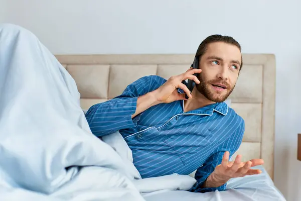 Um homem deitado na cama, a falar ao telemóvel de manhã. — Fotografia de Stock