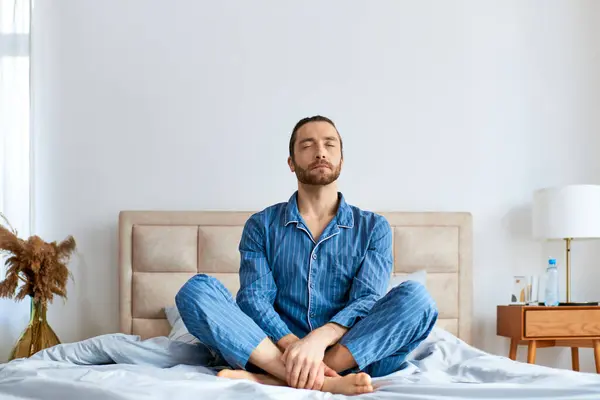 Schöner Mann praktiziert morgens Yoga mit überkreuzten Beinen auf dem Bett. — Stockfoto