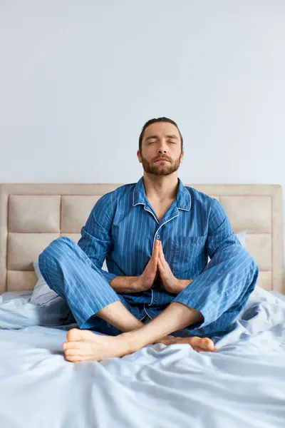 Hombre guapo sentado en la cama, profundamente en la práctica de yoga. - foto de stock
