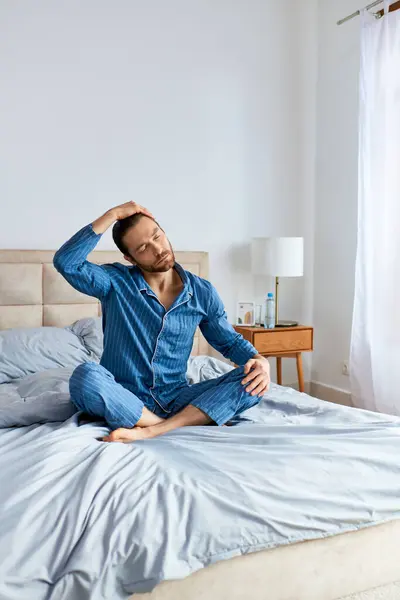 A man in pajamas sits calmly on top of a bed, practicing yoga poses. — Stock Photo