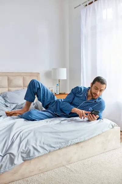 Un uomo pratica pacificamente yoga su un letto mentre è assorto nel suo cellulare. — Foto stock