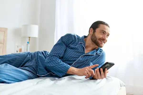 Un homme paisiblement engagé avec son téléphone portable tout en étant allongé sur un lit confortable. — Photo de stock