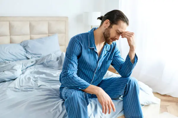Un bell'uomo in pigiama si siede pacificamente su un letto. — Foto stock