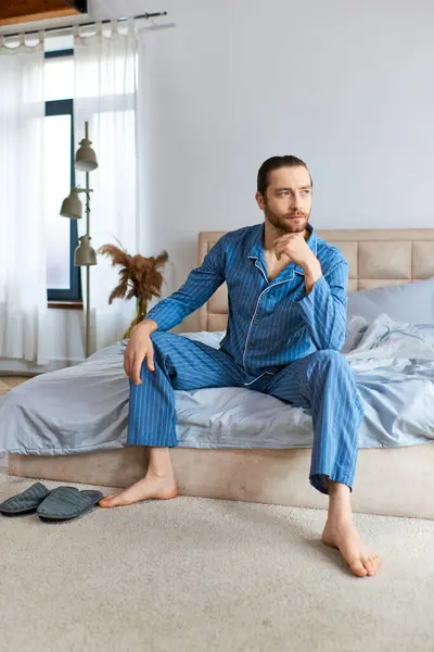 A handsome man in pajamas sits calmly on a bed. — Stock Photo