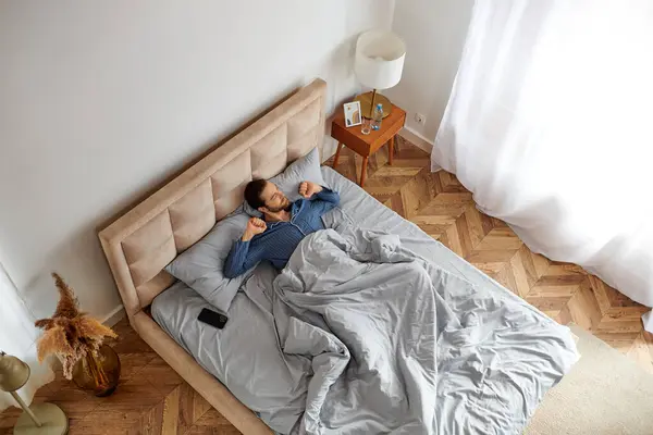 A person peacefully lying in bed with a cozy blanket. — Stock Photo