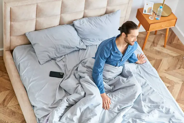 A man in a blue shirt on a bed during a peaceful morning. — Stock Photo