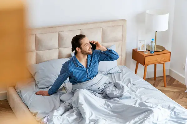 Un uomo si siede su un letto impegnato in una telefonata. — Foto stock