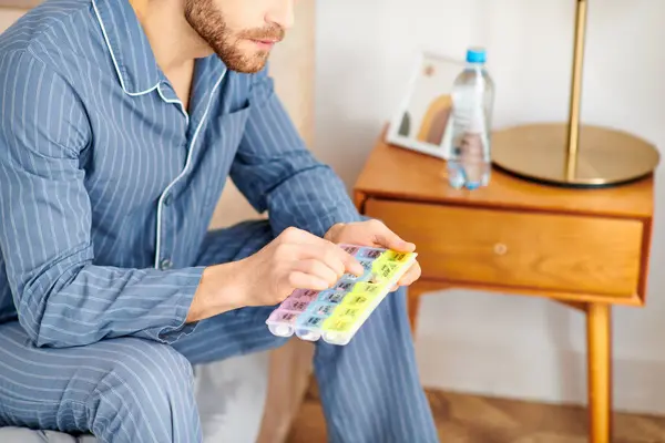 Ein Mann im Schlafanzug entspannt auf einem Bett, in der Hand ein Tablettenetui. — Stockfoto