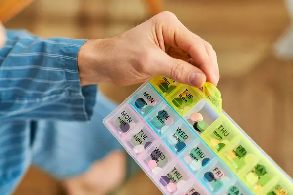 Un hombre guapo en casa por la mañana, sosteniendo pacíficamente un organizador de pastillas de plástico. — Stock Photo