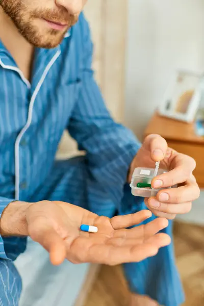 Un hombre se sienta en una cama, en el fondo del pensamiento, sosteniendo un frasco de pastillas. - foto de stock