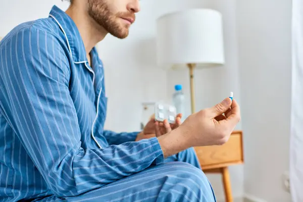 A man seated on a bed, taking pill in a cozy morning atmosphere. — Stock Photo