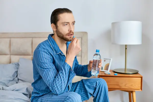 Hombre sentado en la cama, sosteniendo la botella de agua y la píldora, profundamente en el pensamiento. - foto de stock