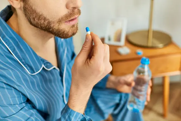Красивый мужчина в синей рубашке с бутылкой воды и таблетками. — стоковое фото