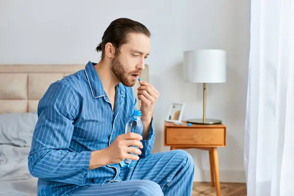Un homme assis paisiblement sur un lit tenant une bouteille d'eau et une pilule. — Photo de stock