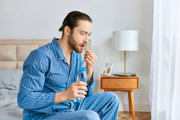 Un uomo si siede pacificamente su un letto con una bottiglia d'acqua e una pillola. — Foto stock