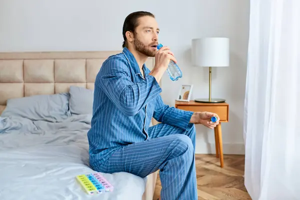 Un uomo seduto su un letto, idratato con acqua da una bottiglia. — Foto stock