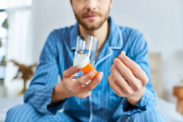 A man in pajamas serenely holds a glass of liquid and taking pills. — Stock Photo