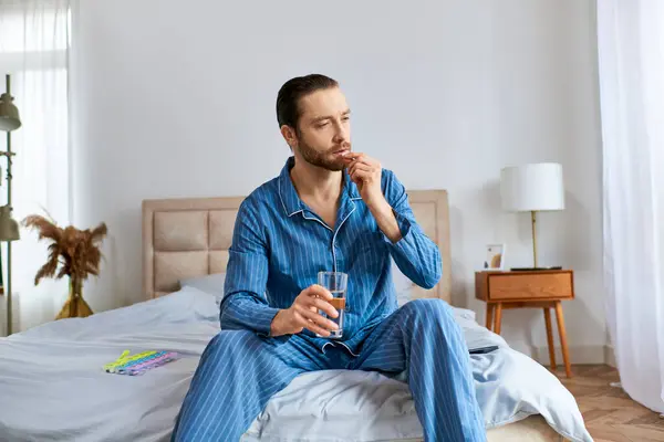Uomo seduto sul letto, che beve un bicchiere d'acqua. — Foto stock