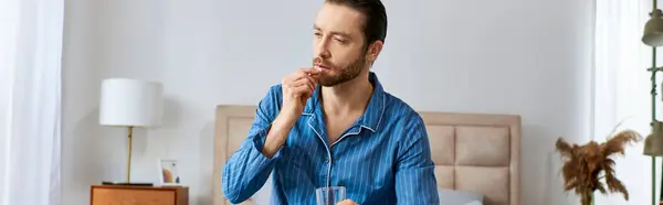 Ein Mann sitzt an einem Tisch, vor sich ein Glas Wasser und nimmt Tabletten. — Stockfoto