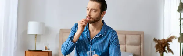 A man is seated at a table with a glass of water in front of him and taking pills. — Stock Photo