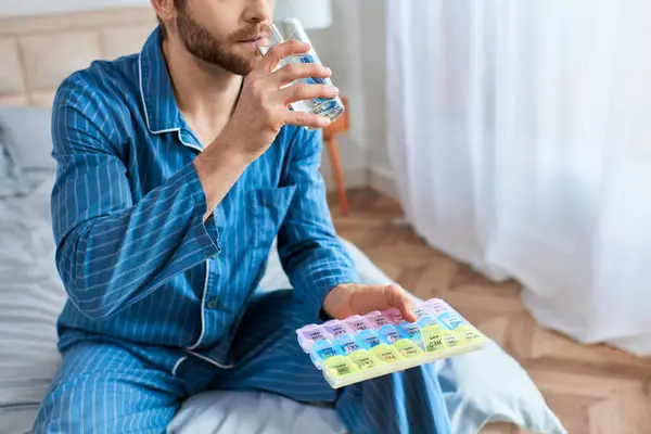 Um homem em ioga posar na cama, saboreando um copo de água e pílulas. — Fotografia de Stock