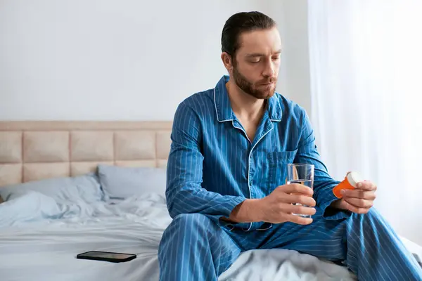 Um homem sentado em uma cama, segurando um copo de água. — Fotografia de Stock