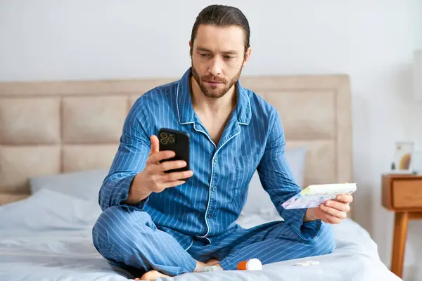 A man, handsome and relaxed, sits on a bed in the morning, focused on his cell phone. — Stock Photo