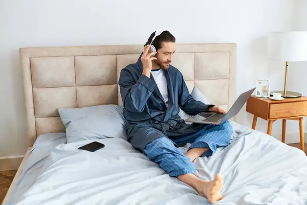 Hombre atractivo en la cama, con auriculares y portátil. - foto de stock
