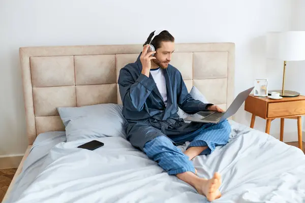 Uomo attraente sul letto, con cuffie e laptop. — Foto stock