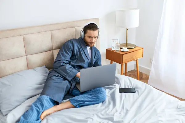 Um homem relaxa em uma cama, usando um laptop em um ambiente tranquilo da manhã. — Fotografia de Stock