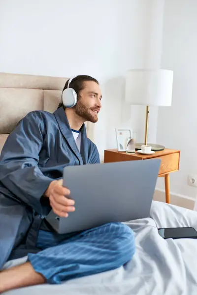 Homem na cama, em fones de ouvido, laptop em uso. — Fotografia de Stock