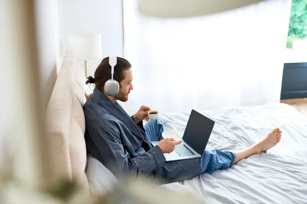 Homem sentado na cama, usando laptop para relaxamento matinal. — Fotografia de Stock