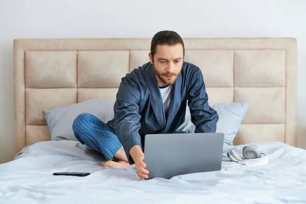 Un homme accroupi dans son ordinateur portable, assis sur un lit. — Photo de stock